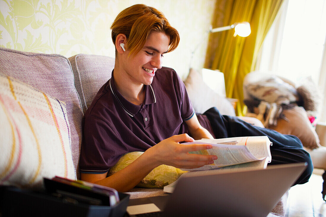 Teenage boy with textbook and laptop studying at home