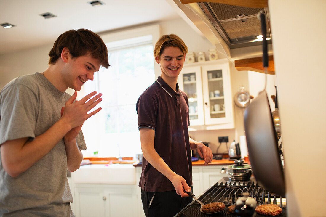 Happy teenage boys grilling hamburgers at kitchen stove