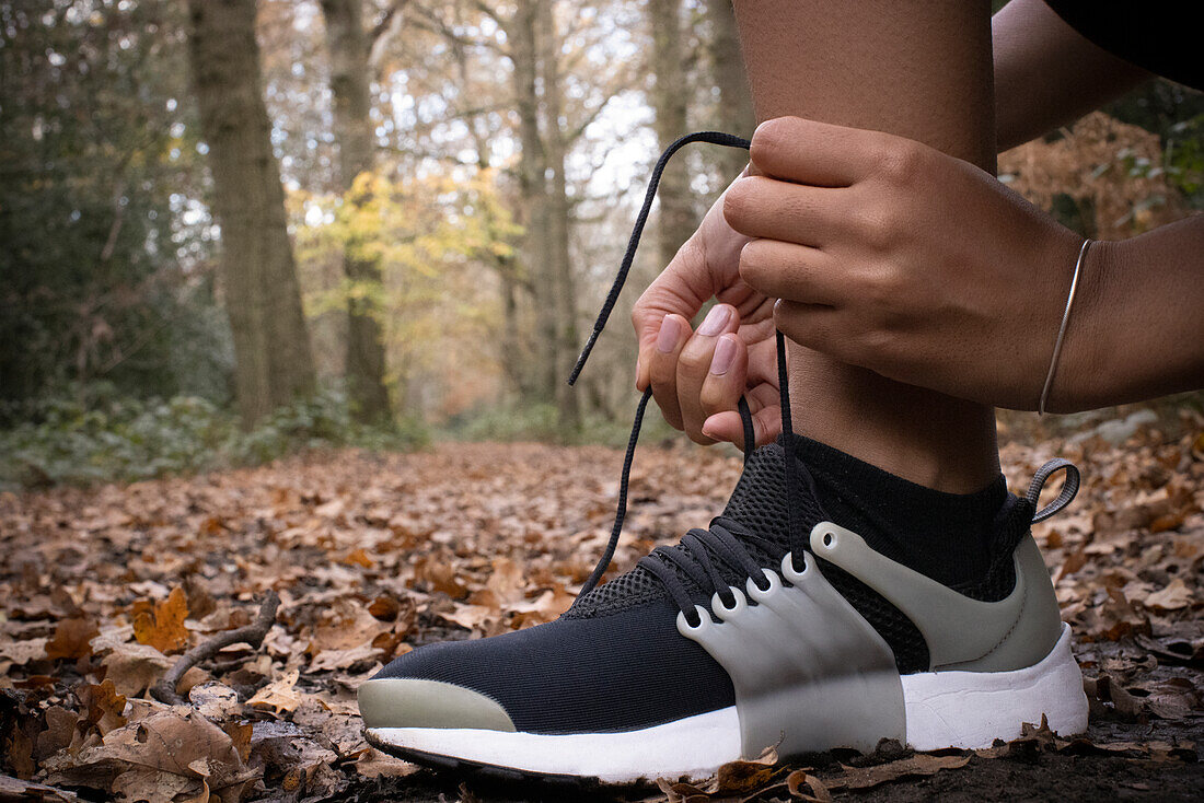 Female runner tying shoelace in autumn woods