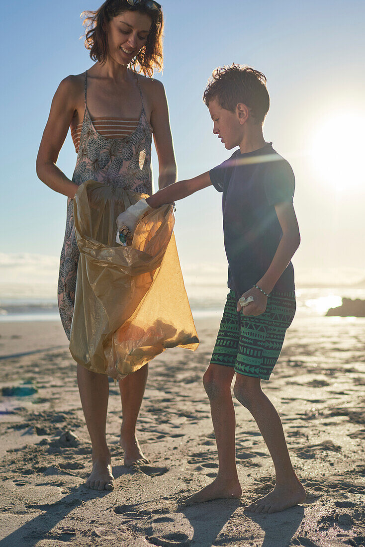 Mother and son picking up garbage on sunny beach