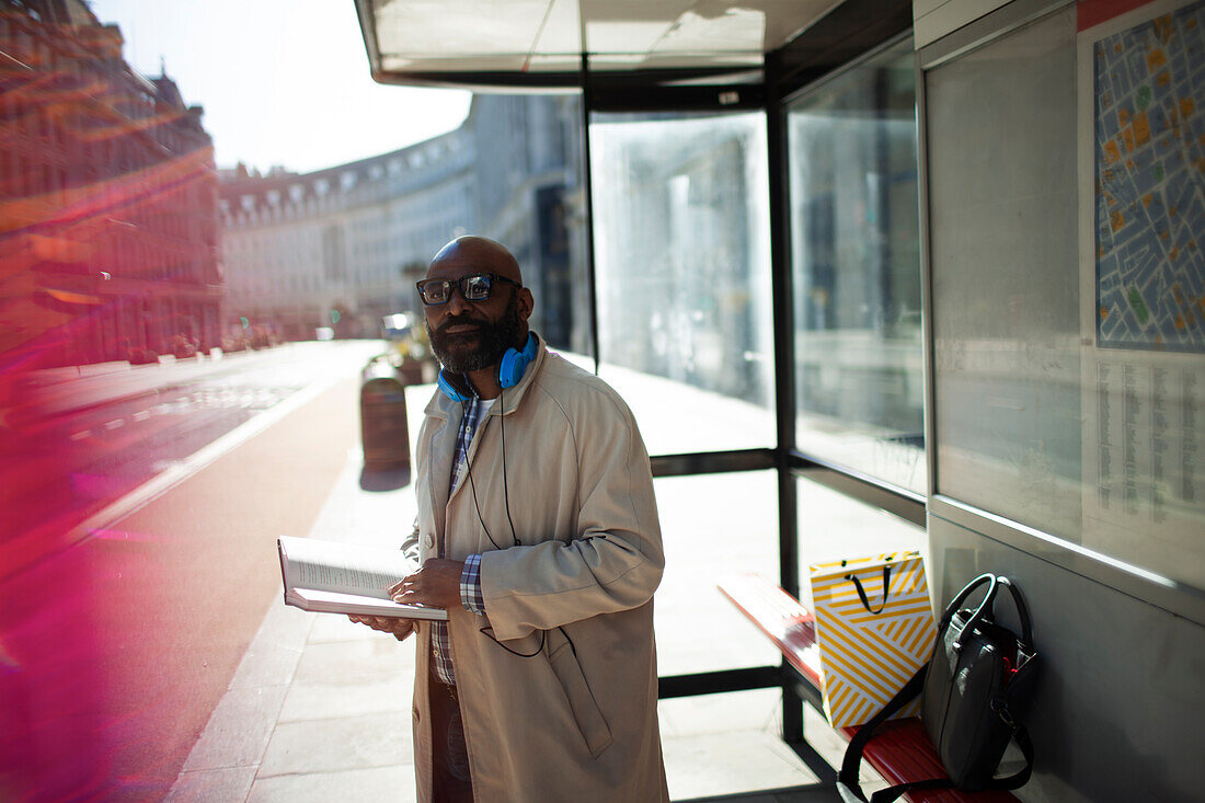 Businessman with book waiting at urban bus stop, London, UK