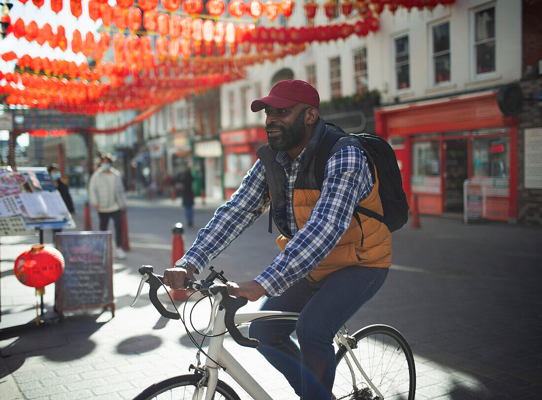 Man riding bike on sunny city street, Chinatown, London, UK