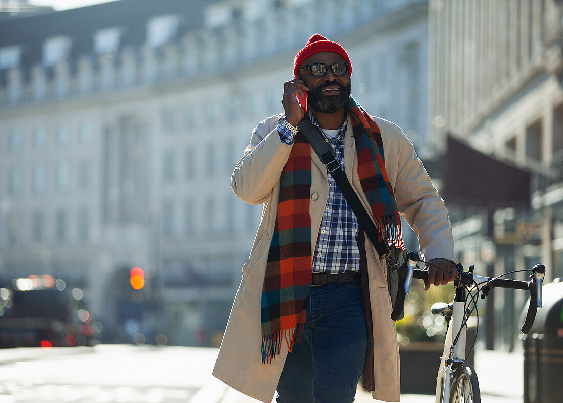 Businessman with bicycle talking on smartphone in sunny city