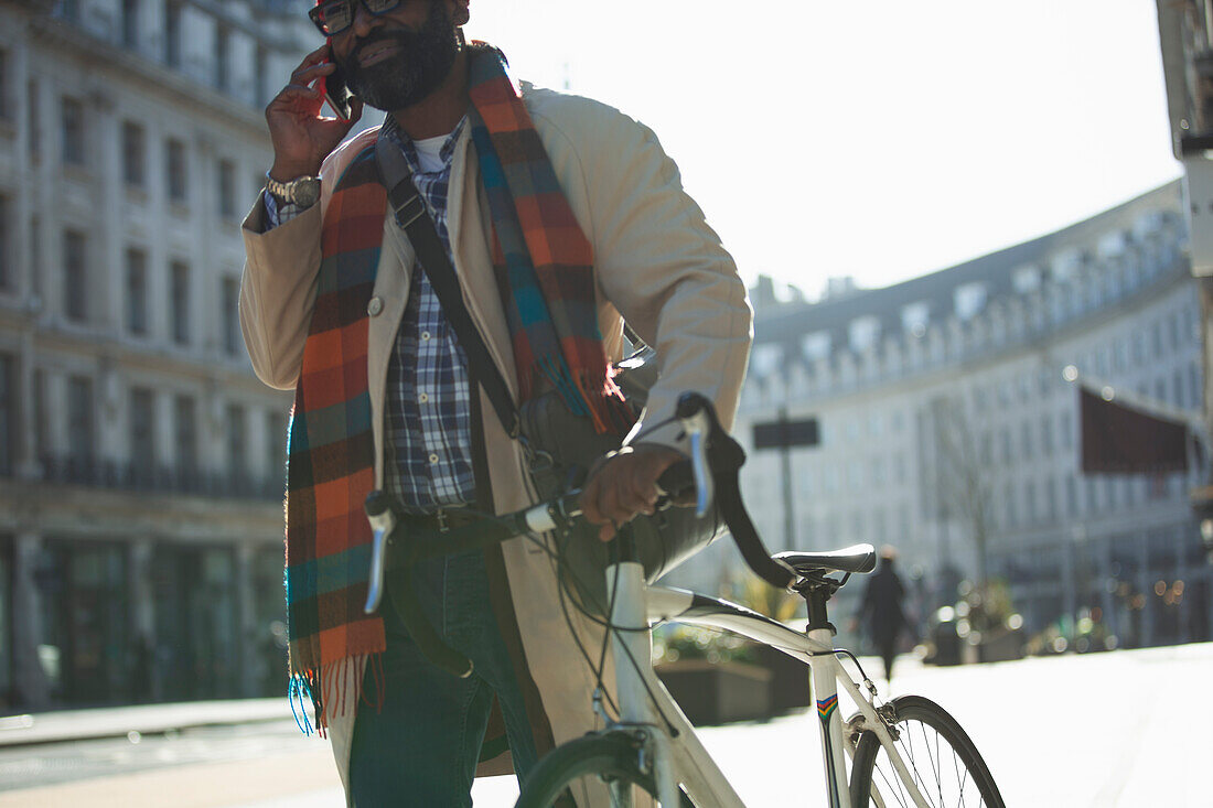 Businessman with bicycle talking on smartphone in sunny city