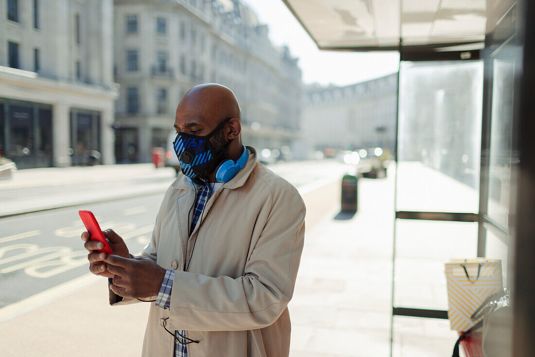 Businessman in face mask using smartphone at city bus stop