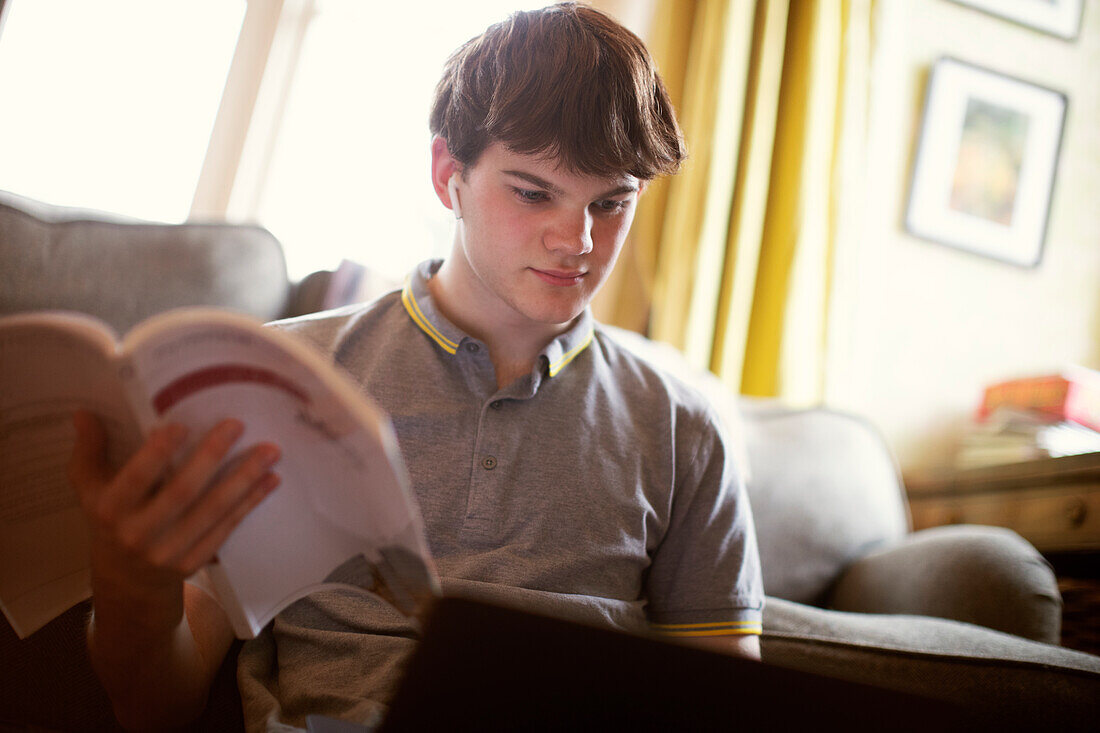 Focused teenage boy with textbook and laptop studying
