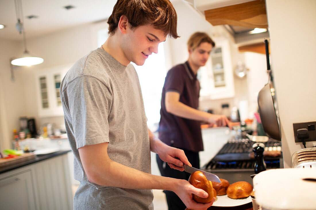 Teenage boy slicing hamburger buns in kitchen