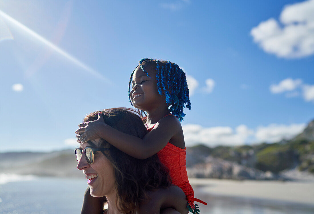 Happy mother carrying daughter on shoulders on sunny beach