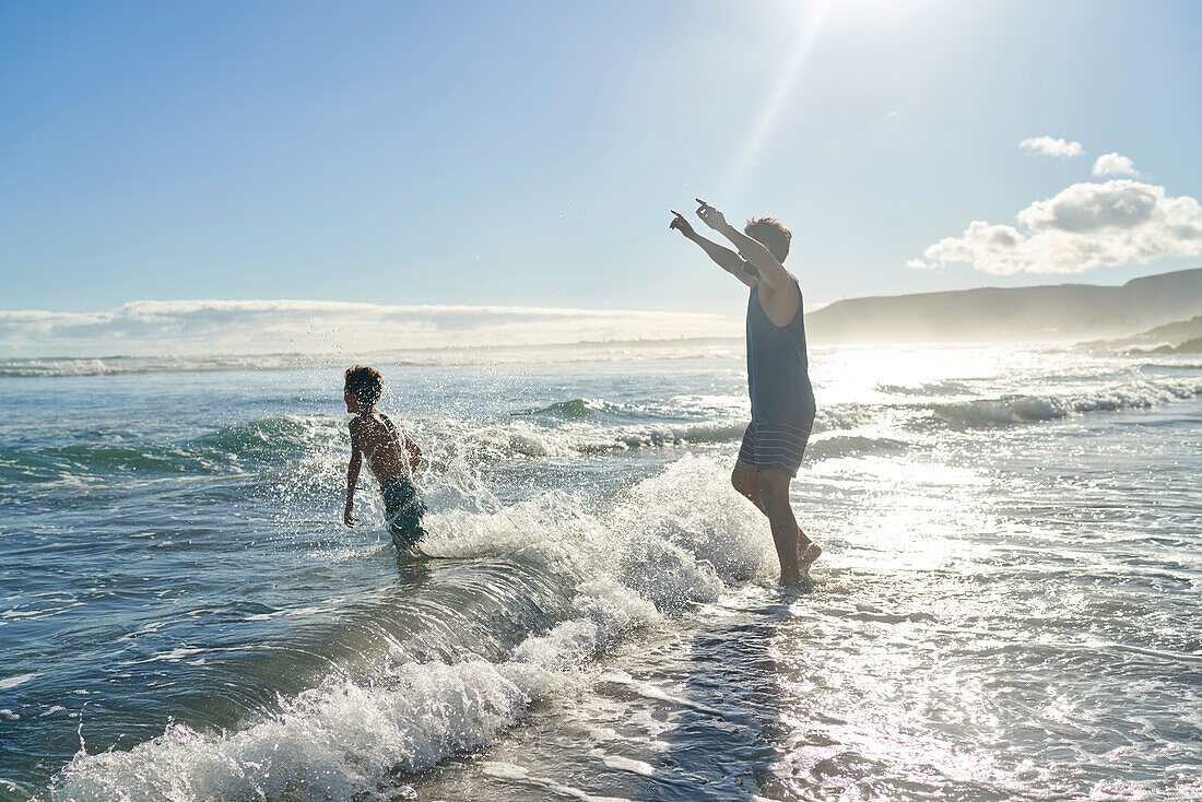 Playful father and son playing in sunny summer ocean surf