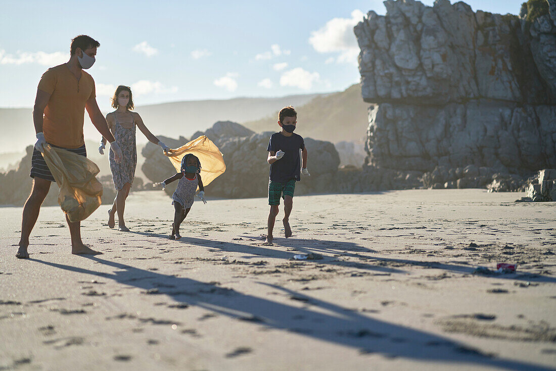 Family in face masks picking up litter on sunny beach