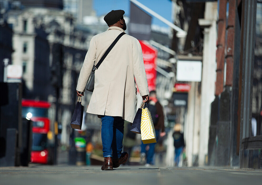 Man in trench coat carrying shopping bags on city sidewalk
