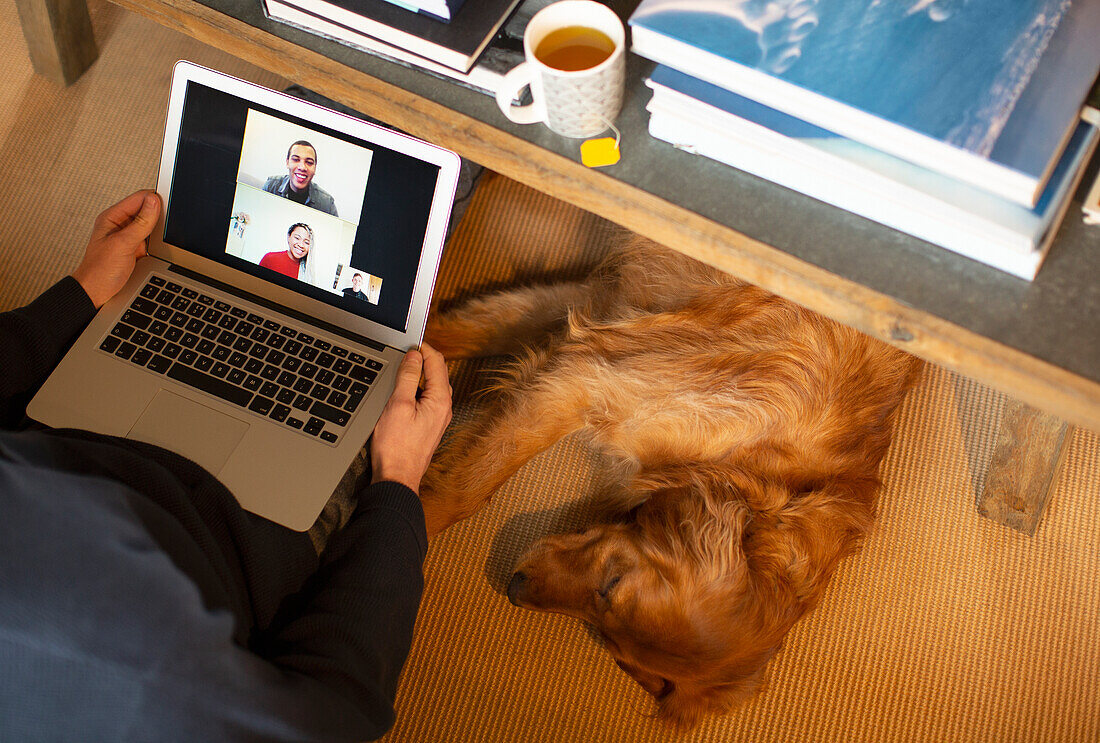 Dog sleeping below man video conferencing with colleagues