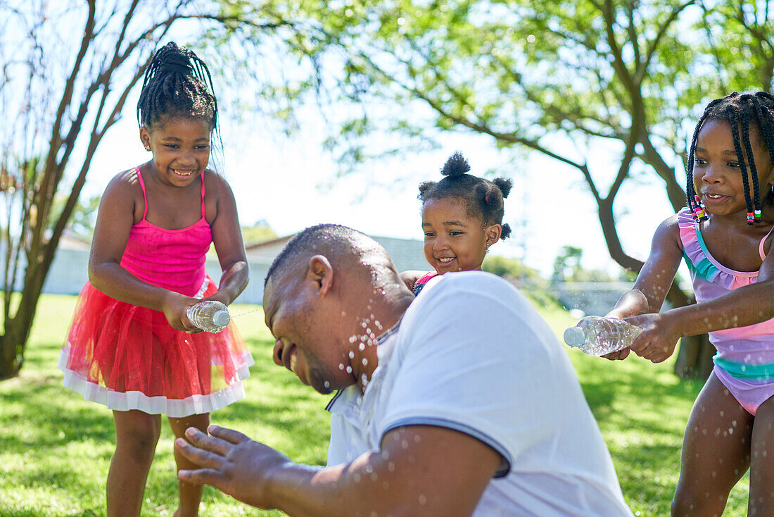 Happy playful daughters splashing father with water bottles