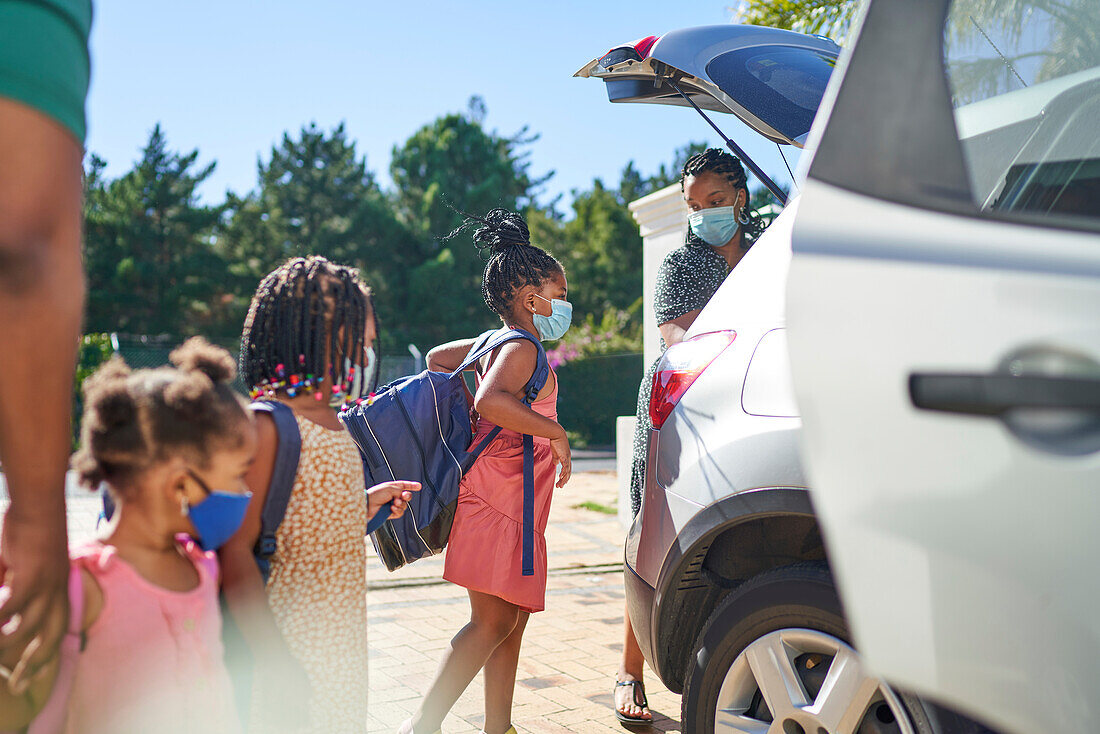 Mother and daughters loading backpacks into car