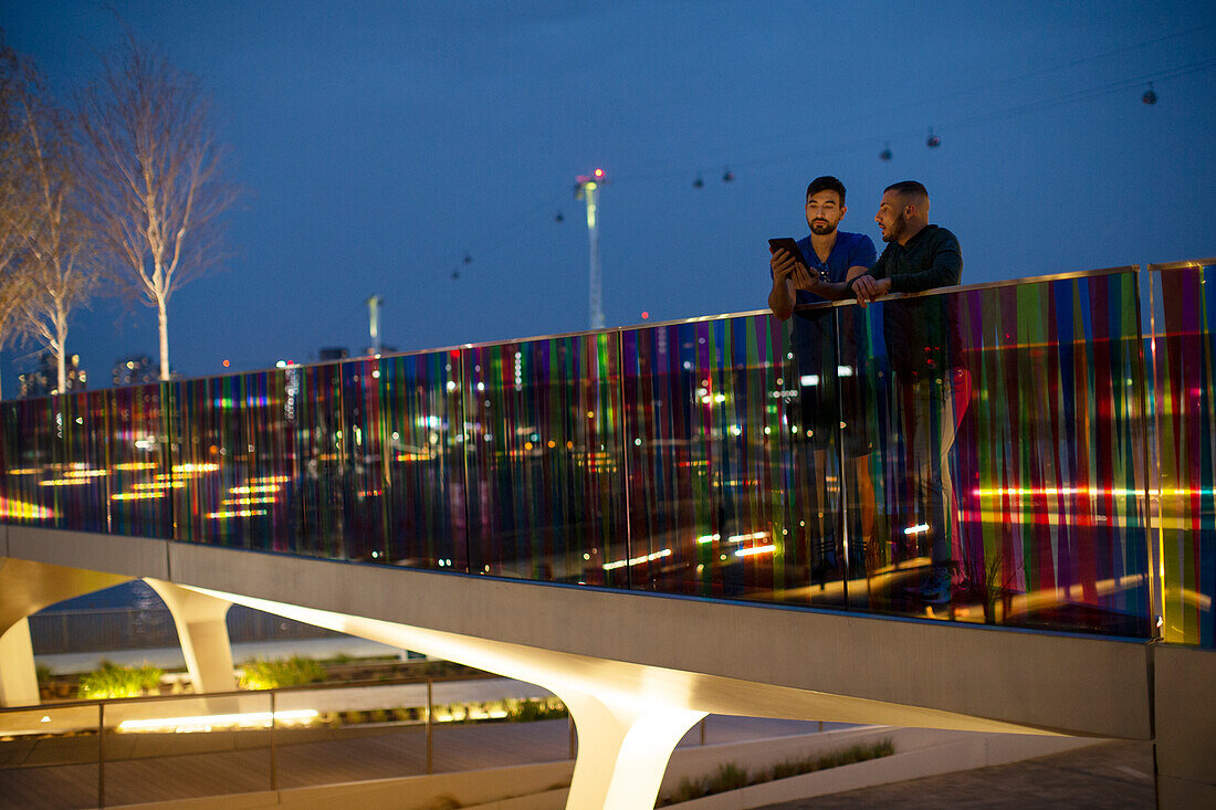 Men talking on illuminated urban footbridge at night