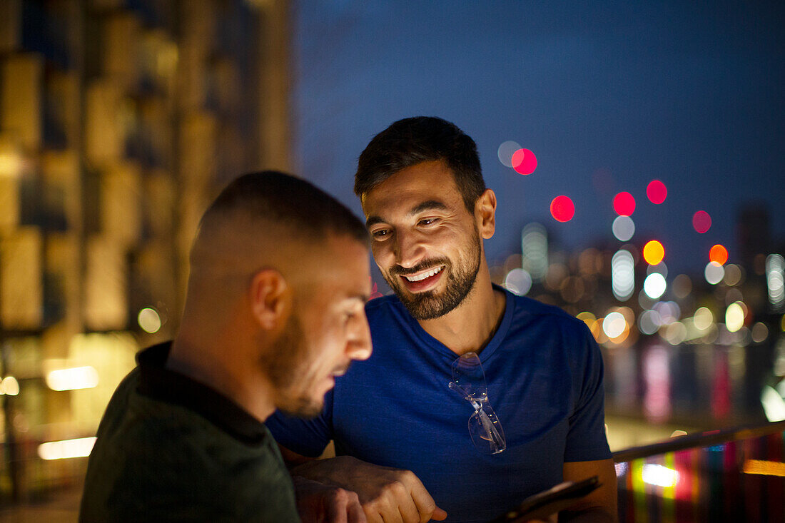 Happy men with smartphone in city at night