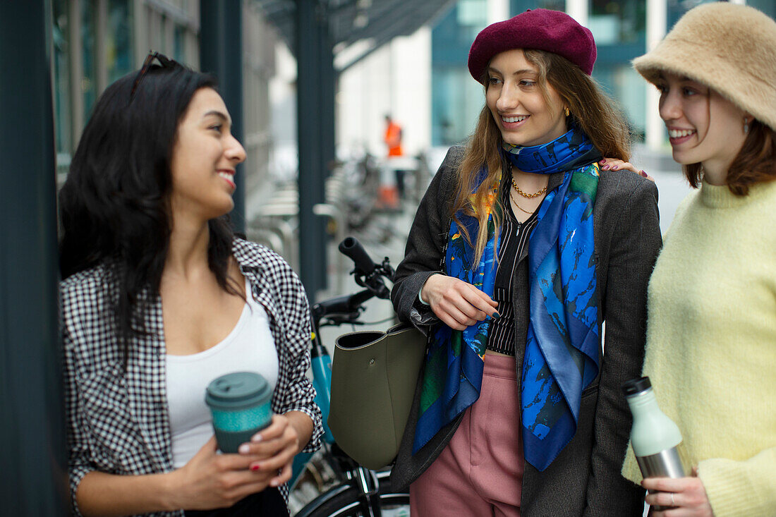 Happy young female friends talking on sidewalk