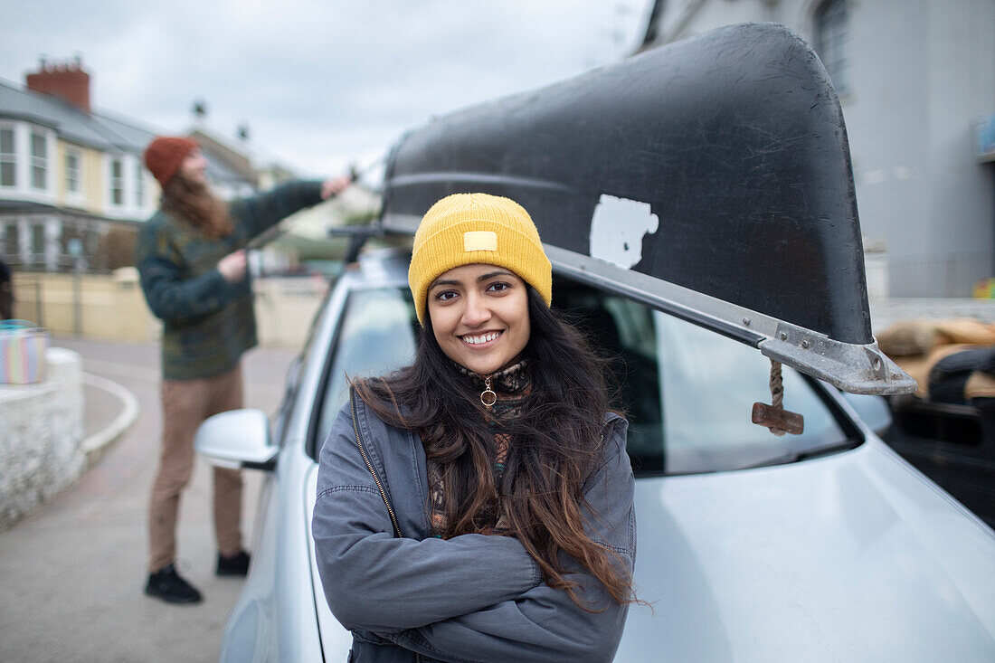 Happy young woman outside car with canoe