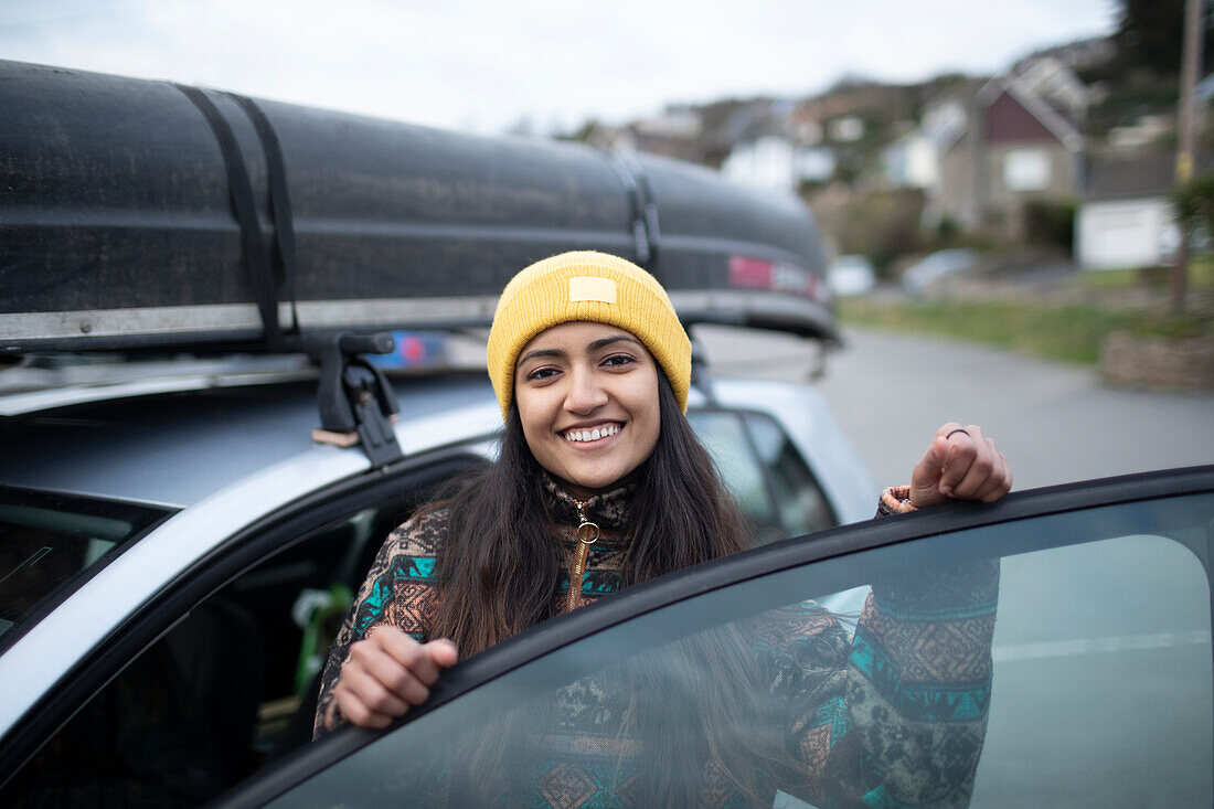 Happy young woman getting into car with canoe on top