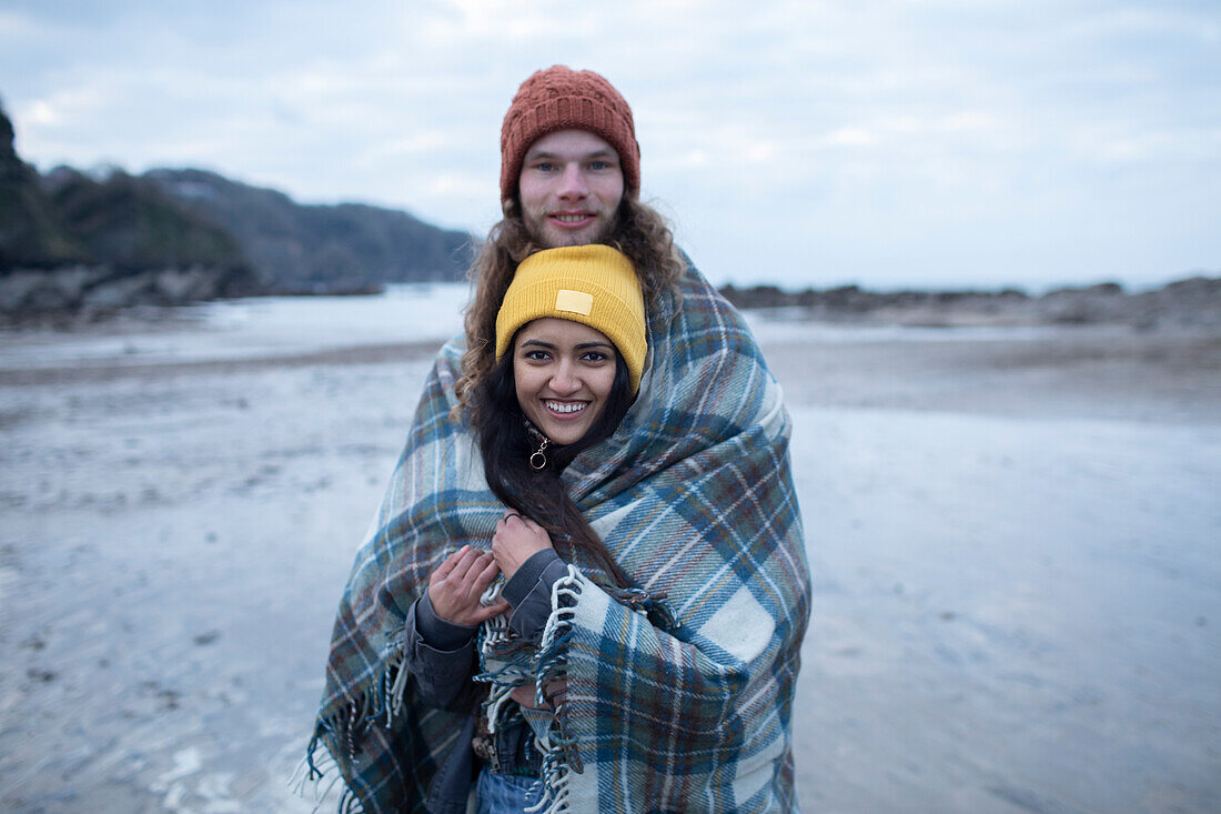 Happy young couple wrapped in blanket on cold beach