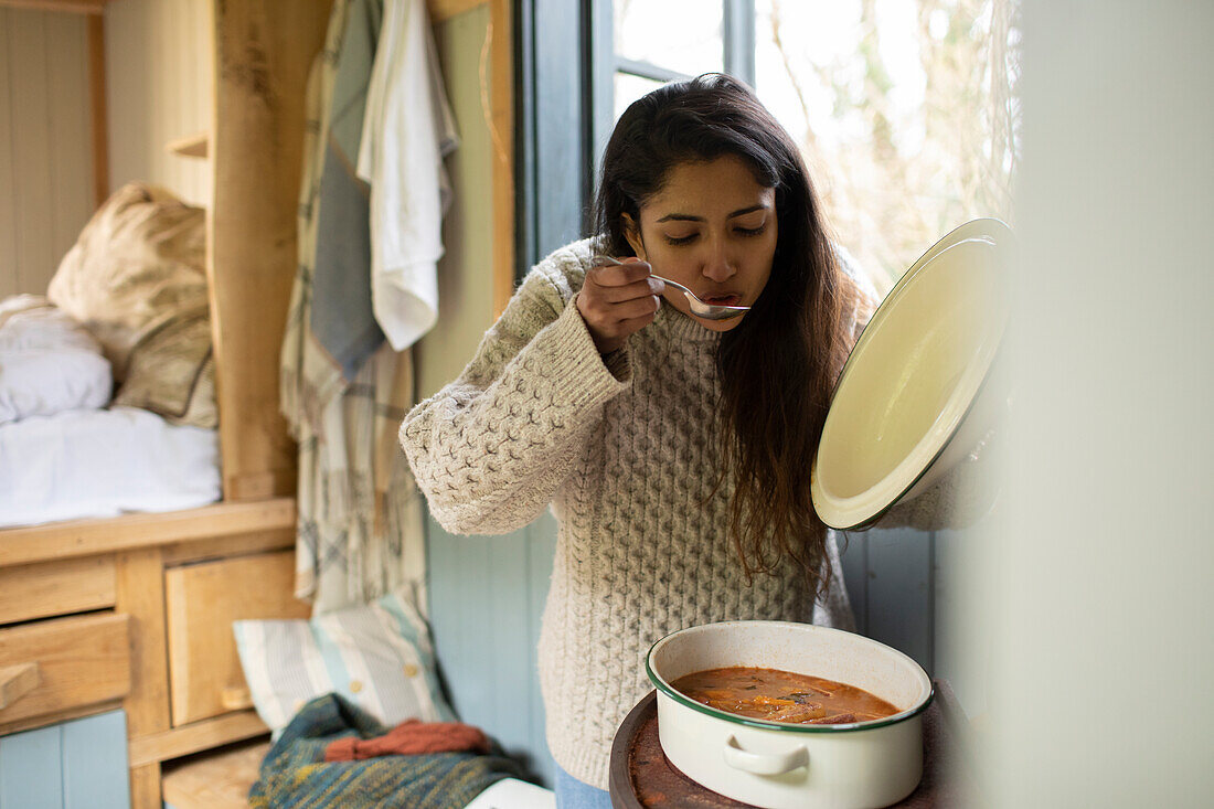 Young woman cooking stew in tiny cabin
