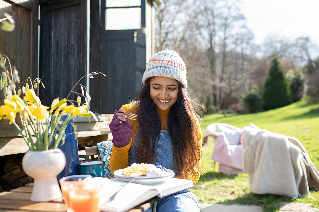 Happy young woman eating at sunny campsite