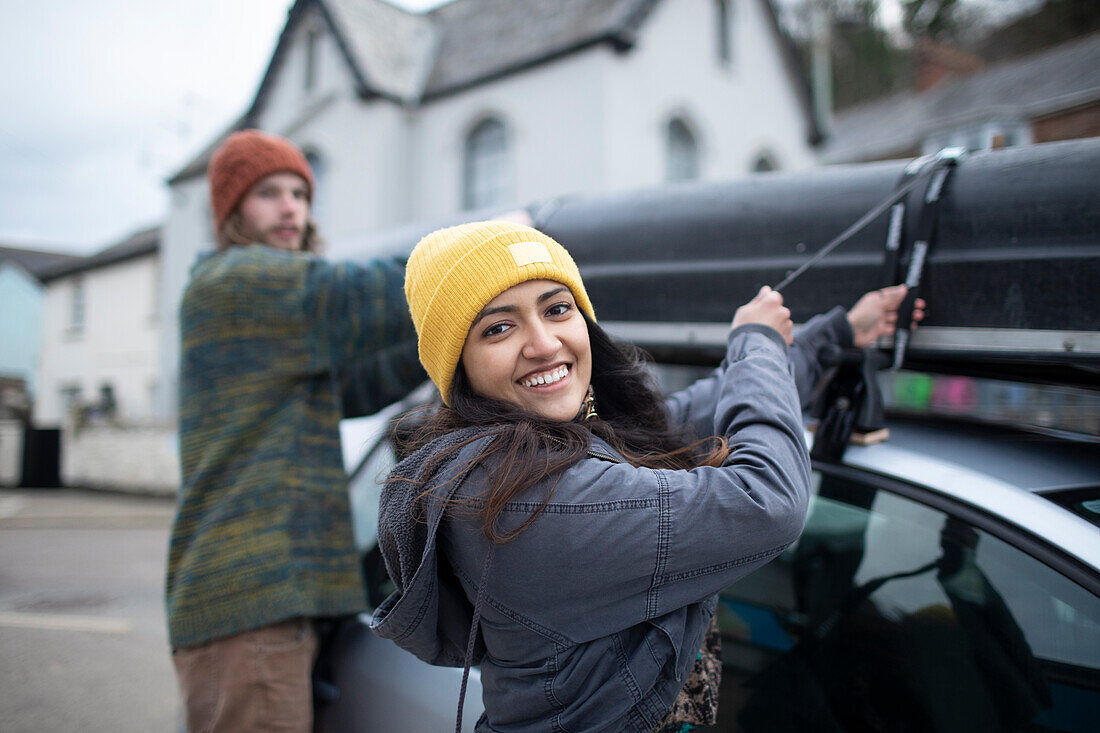 Happy young couple fastening canoe to top of car