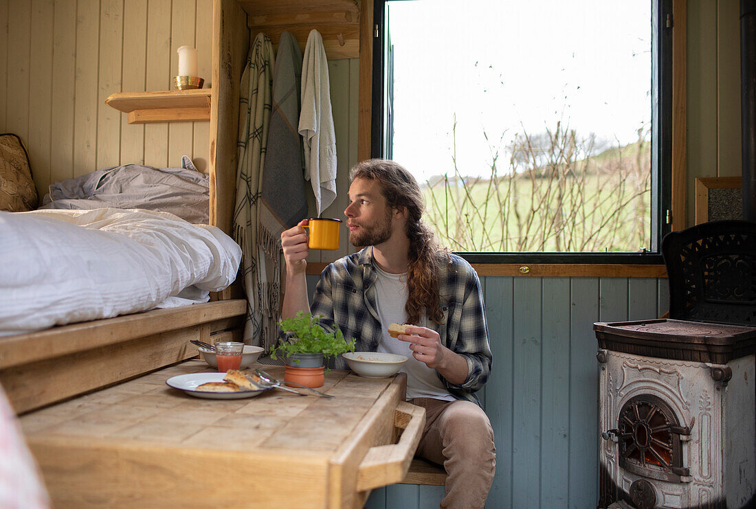 Young man eating and drinking in tiny cabin rental