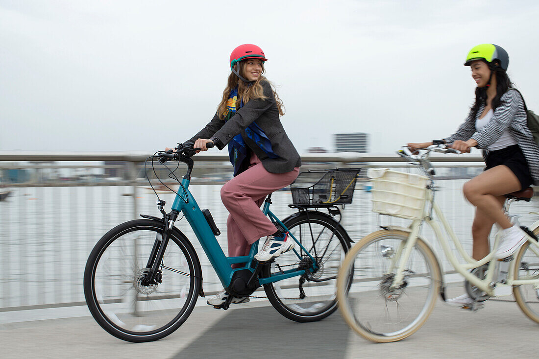 Young female friends riding bicycles on urban bridge