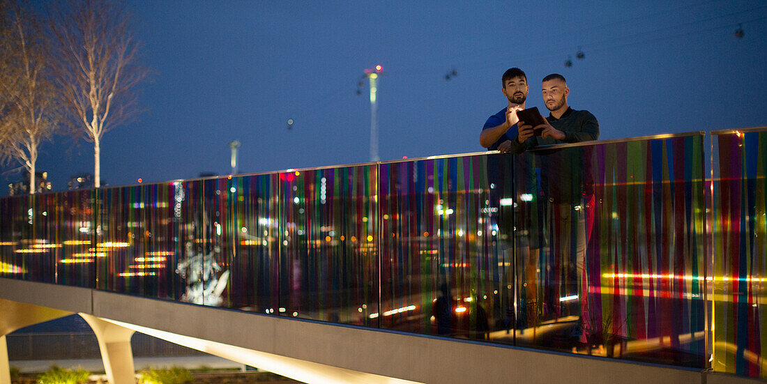 Men with smartphone on footbridge in city at night