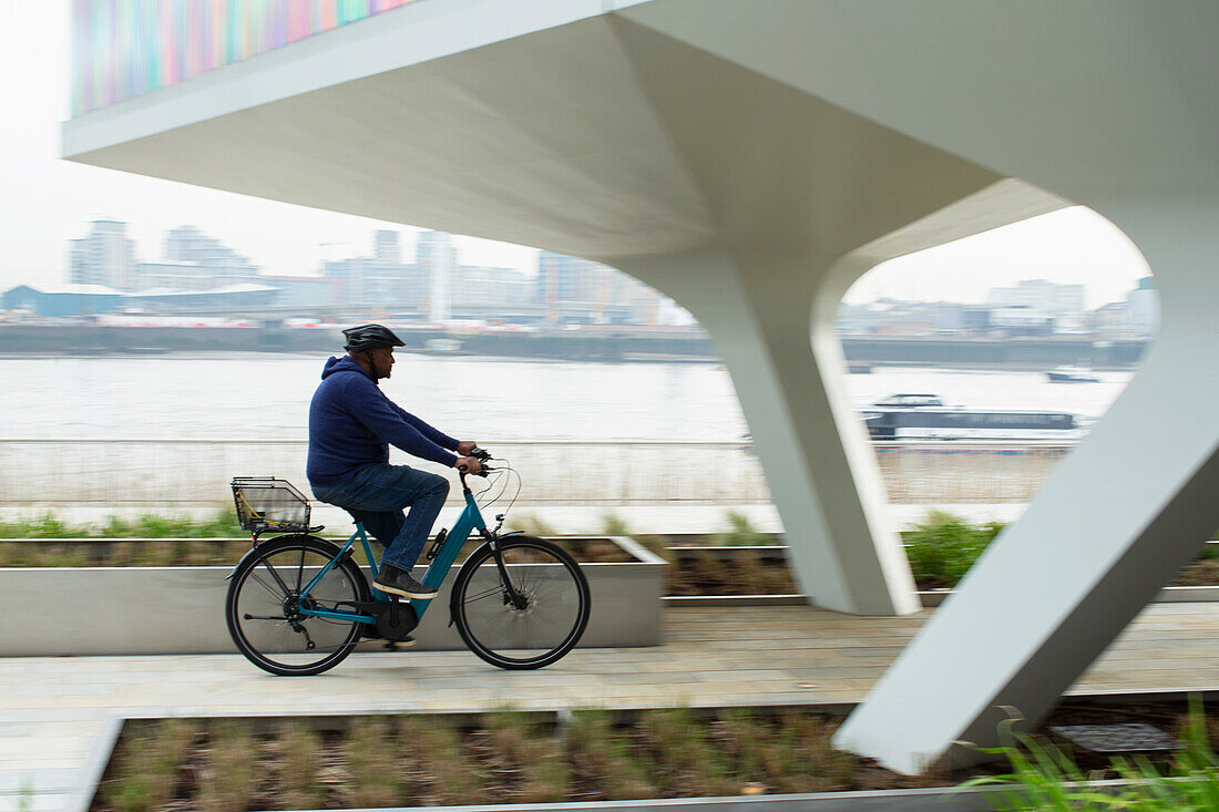 Man riding bicycle on urban waterfront sidewalk, London, UK