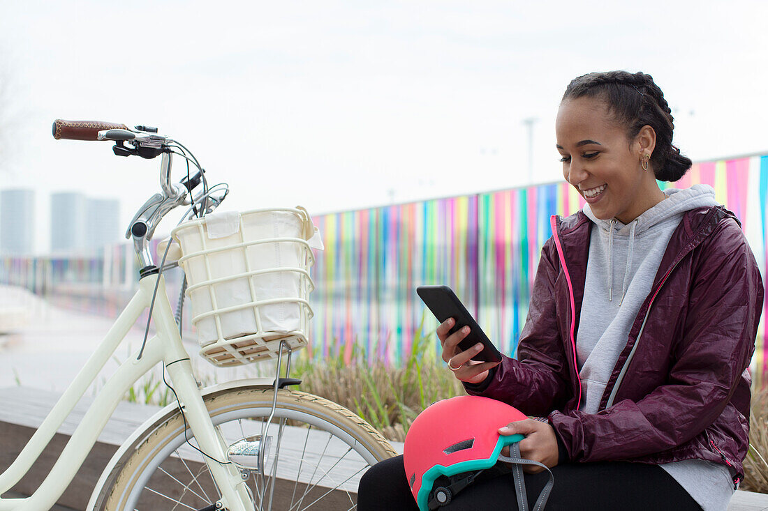 Happy teen girl with bicycle using smartphone