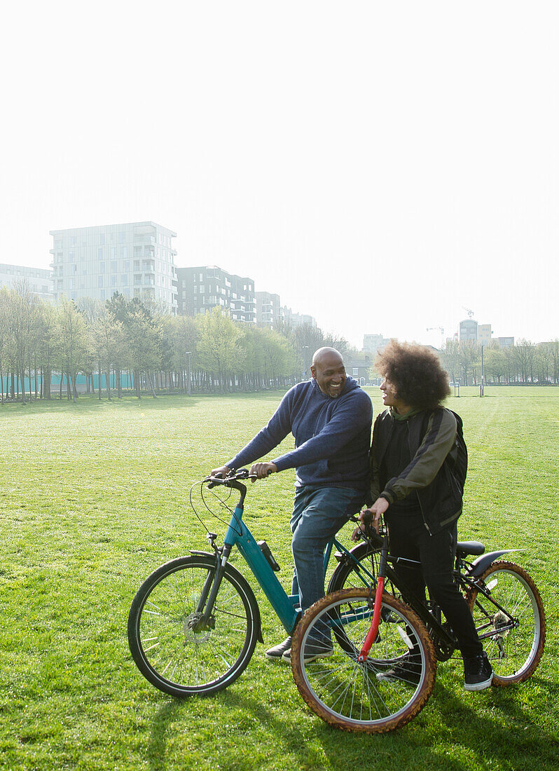 Father and son riding bicycles in sunny urban park