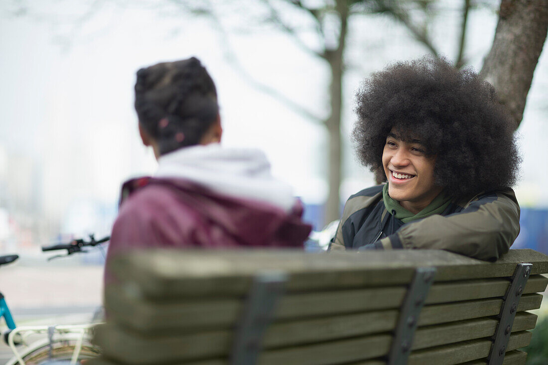Happy young man talking to friend on park bench