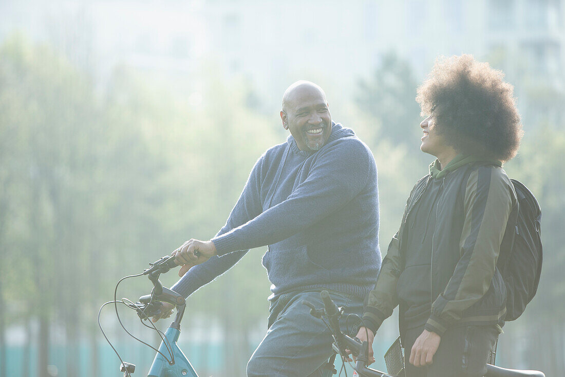 Happy father and teen son on bicycles in park