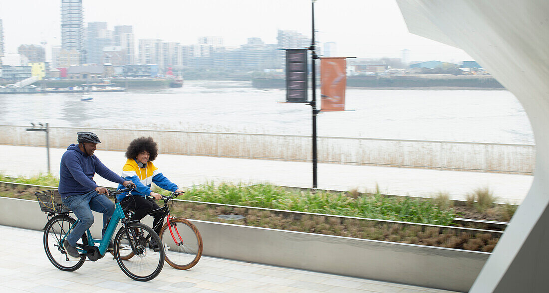 Father and son riding bicycles along waterfront in city