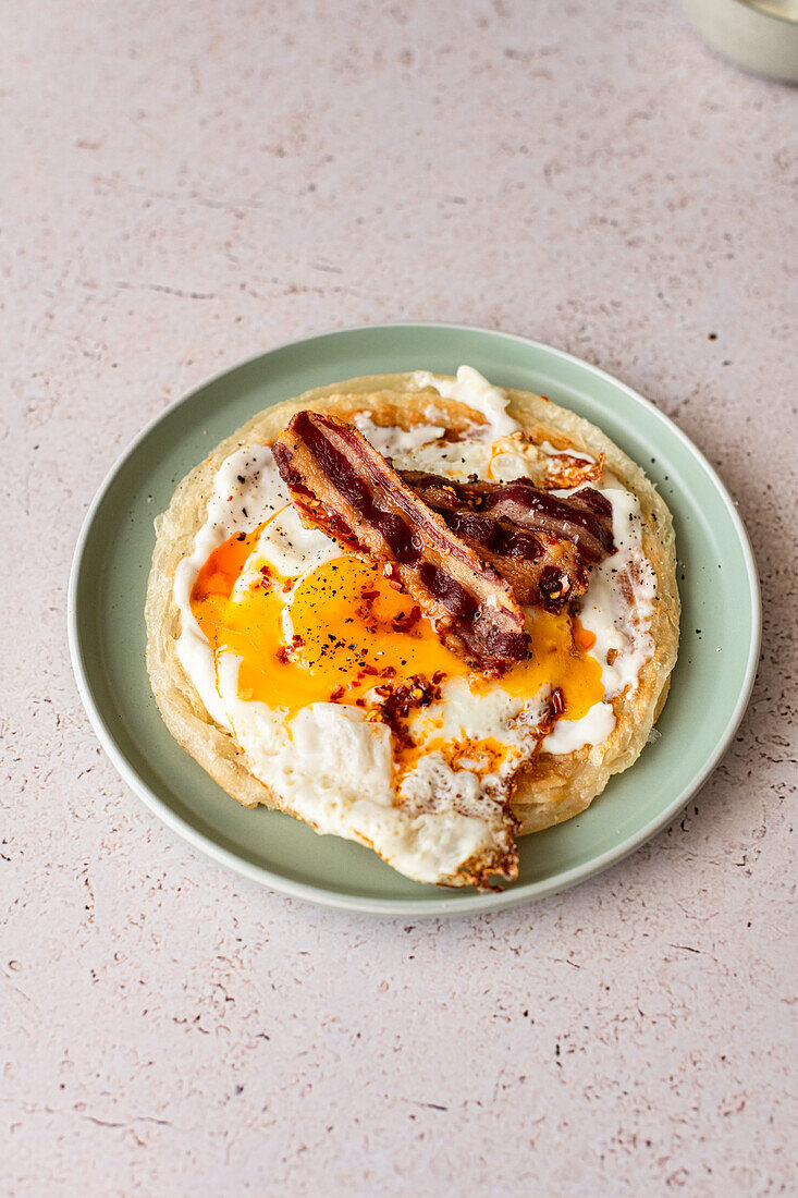 Paratha with garlic yoghurt, runny fried egg, bacon and chilli oil