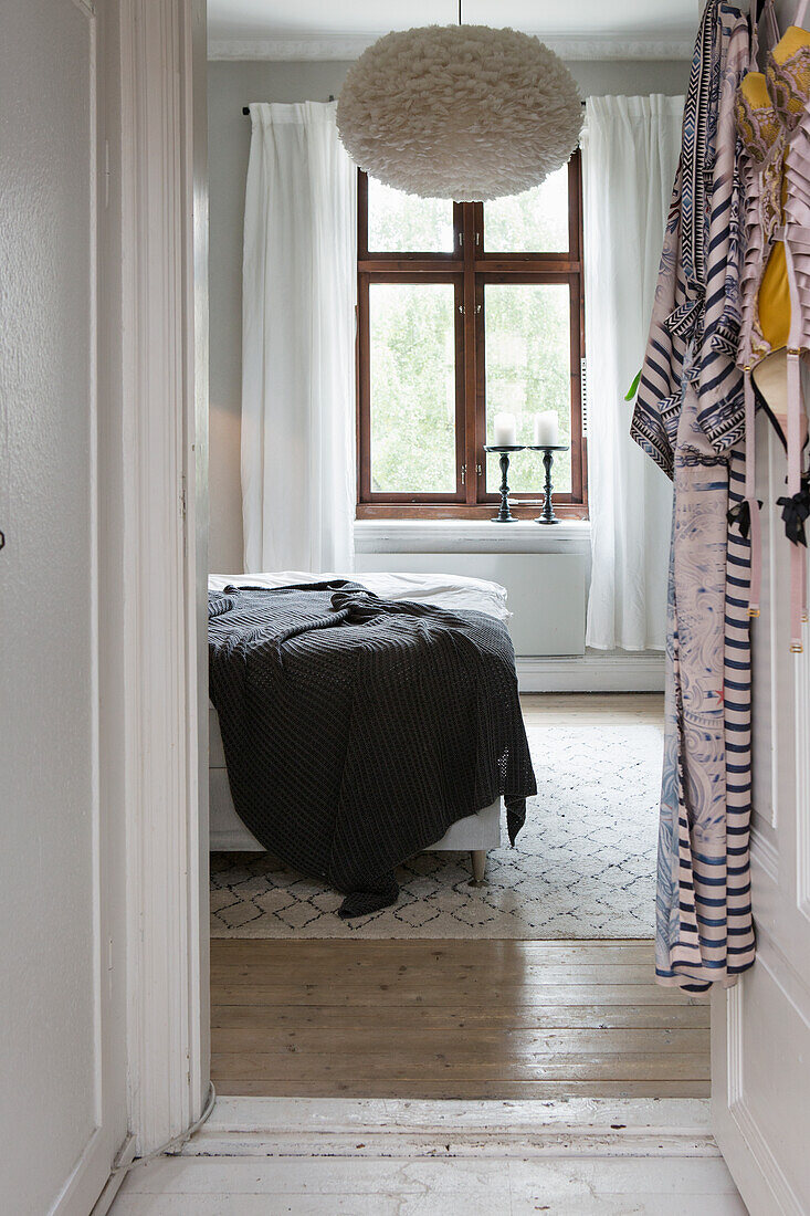 View into the bedroom with large ceiling lamp, white curtains and carpet on wooden floor