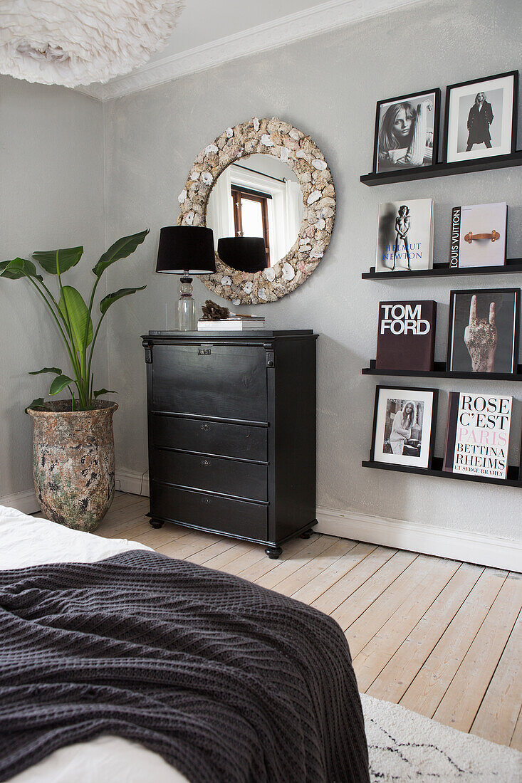 Bedroom with black chest of drawers, wall shelves, round mirror and plant decoration