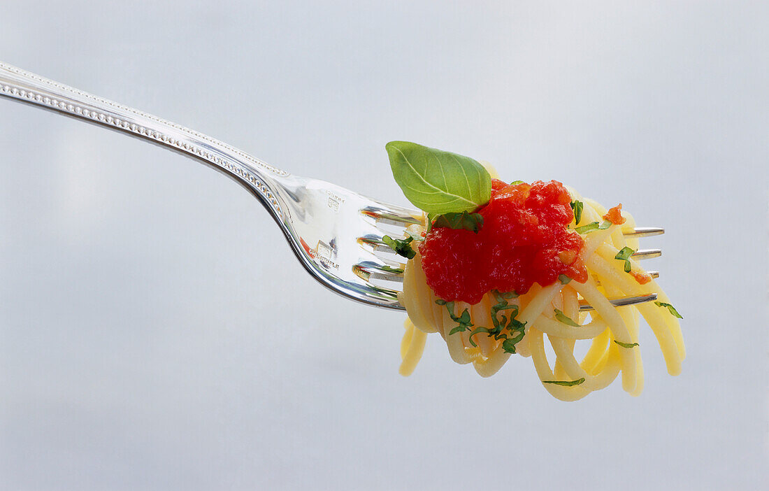 Fork with pasta, tomato sauce and basil