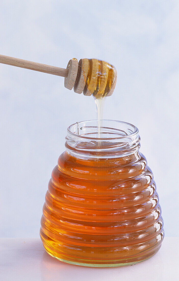 A glass of honey, with a honey dipper