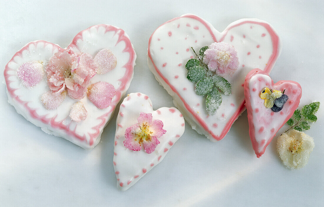 Vier herzförmige Torten zum Valentinstag, mit gezuckerten Rosenblüten