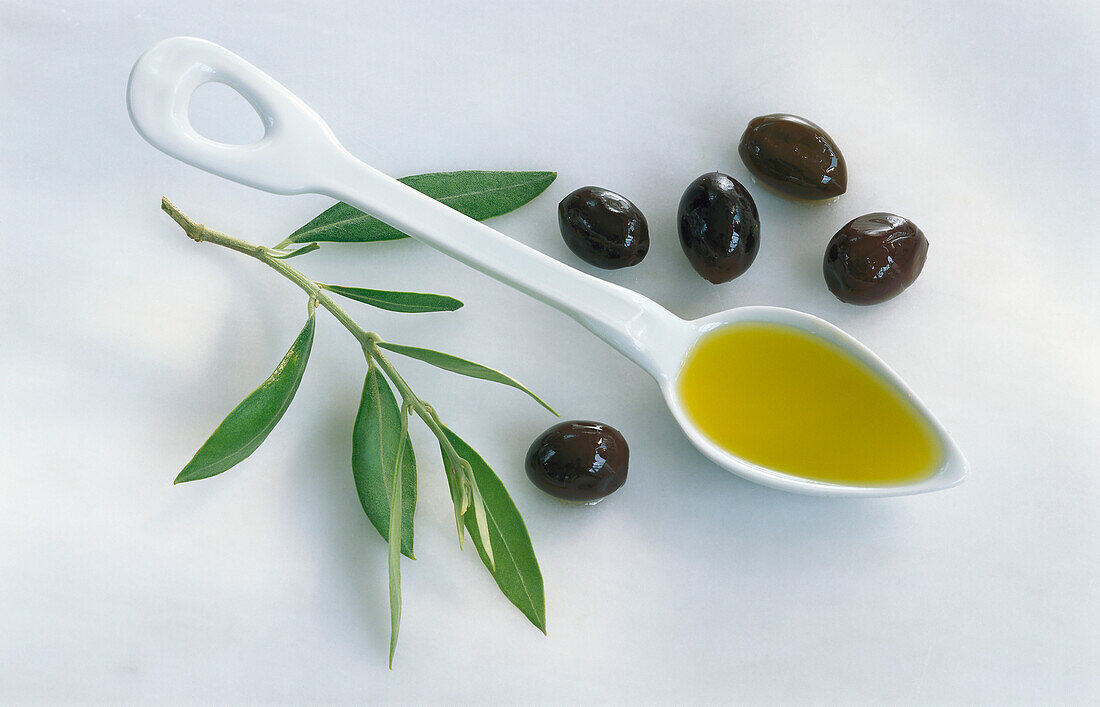 Löffel mit Olivenöl, daneben Oliven