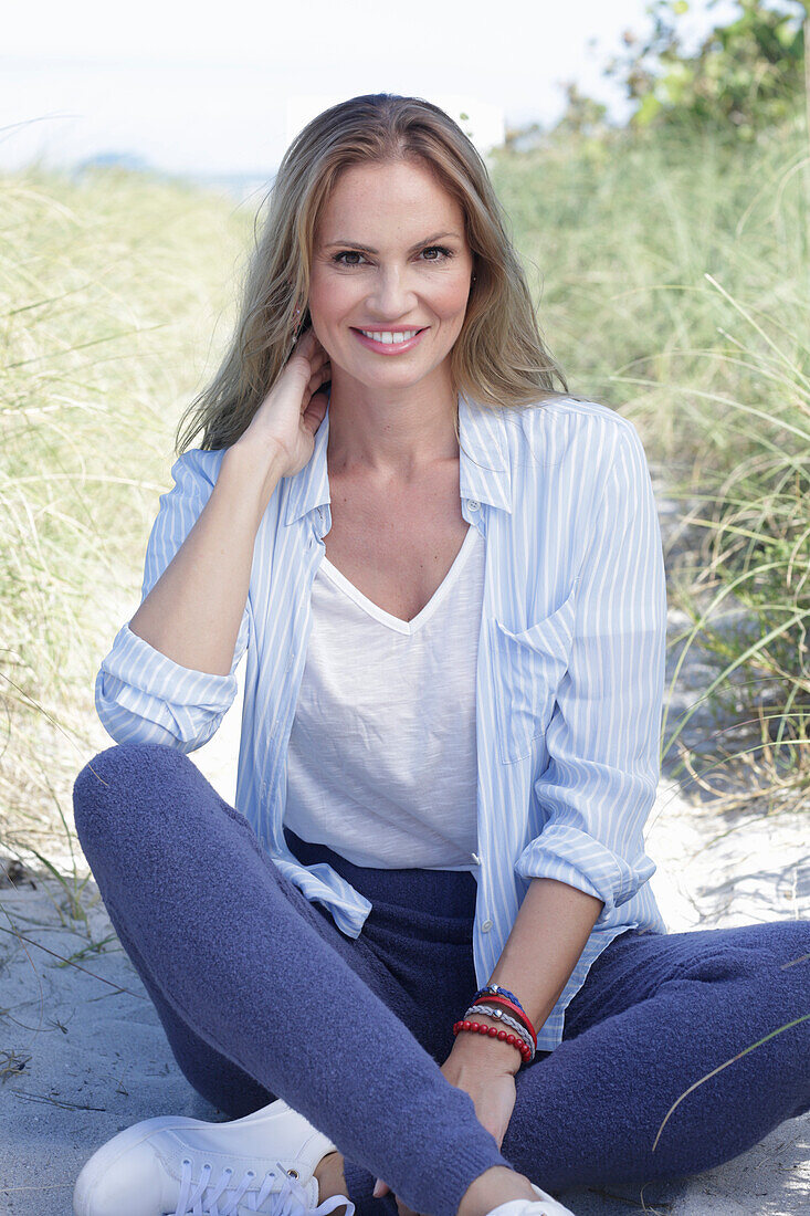 A long-haired woman wearing a spring-like blue-and-white outfit sitting on a beach