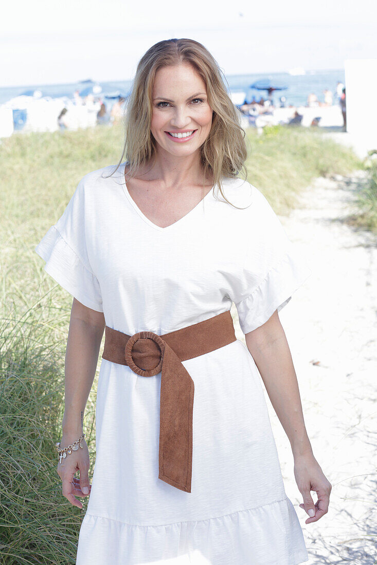 Langhaarige Frau in weißem Sommerkleid mit Gürtel am Strand