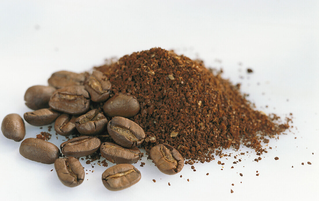 Coffee beans and a heap of coffee powder on a light background