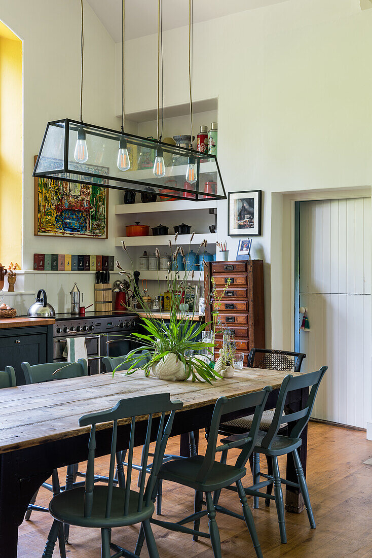 Kitchen with dining table with dark green chairs and elongated glass pendant light