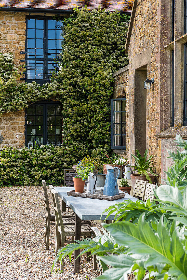 Idyllische Terrasse mit Gartentisch vor historischem Gebäude mit Efeubewuchs