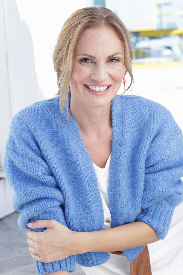 Langhaarige Frau in weißem Sommerkleid und blauer Strickjacke am Strand