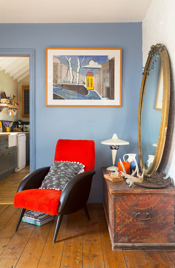 Vintage-Wohnzimmer mit blauer Wand, rotem Sessel, rundem Spiegel und antiker Truhe